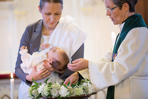 Pappi, sylikummi ja kastettava lapsi kastetilaisuudessa