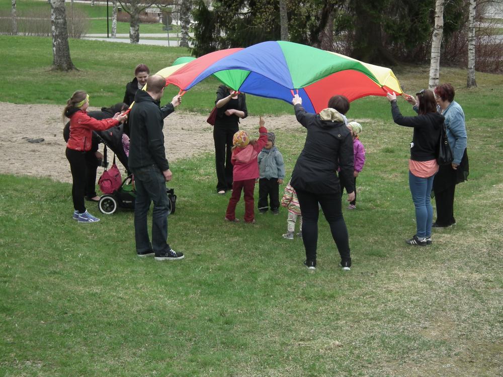 Lapsia ja aikuisia leikkimässä sateenkaari varjolla